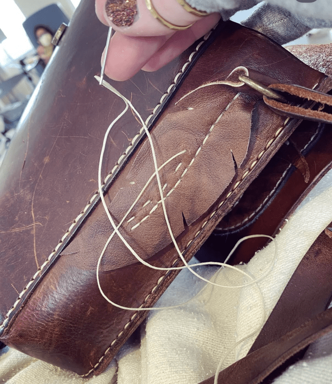 A close up of a brown leather bag with fingers sewing a leather feather shaped piece to the bag.